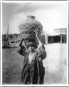 Apache girl balances water basket on head